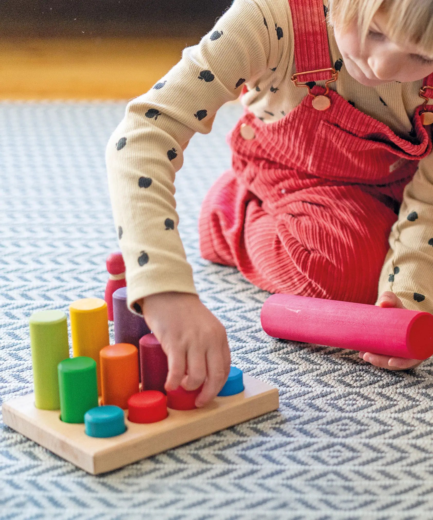 Child sorting individual Grimms small wooden stacking rollers in its sorting tray and holding a large roller showing scale