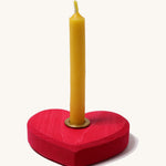 Grimm's Small Red Heart with a brass candle holder and candle on a plain background. 