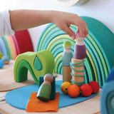 Small child's hand holding a peg doll standing on loose Grimms small world play in the woods blocks showing scale