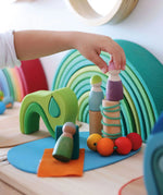 Small child's hand holding a peg doll standing on loose Grimms small world play in the woods blocks showing scale