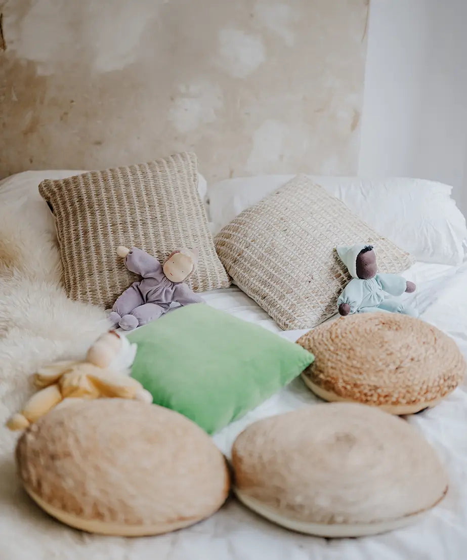 A violet, aqua and yellow Grimms soft Waldorf doll on a bed