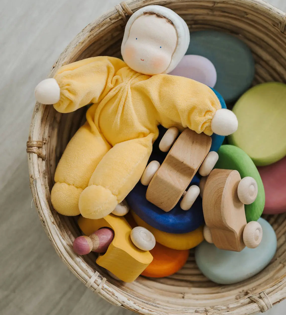 A Grimms yellow soft Waldorf doll in a basket filled with wooden toys