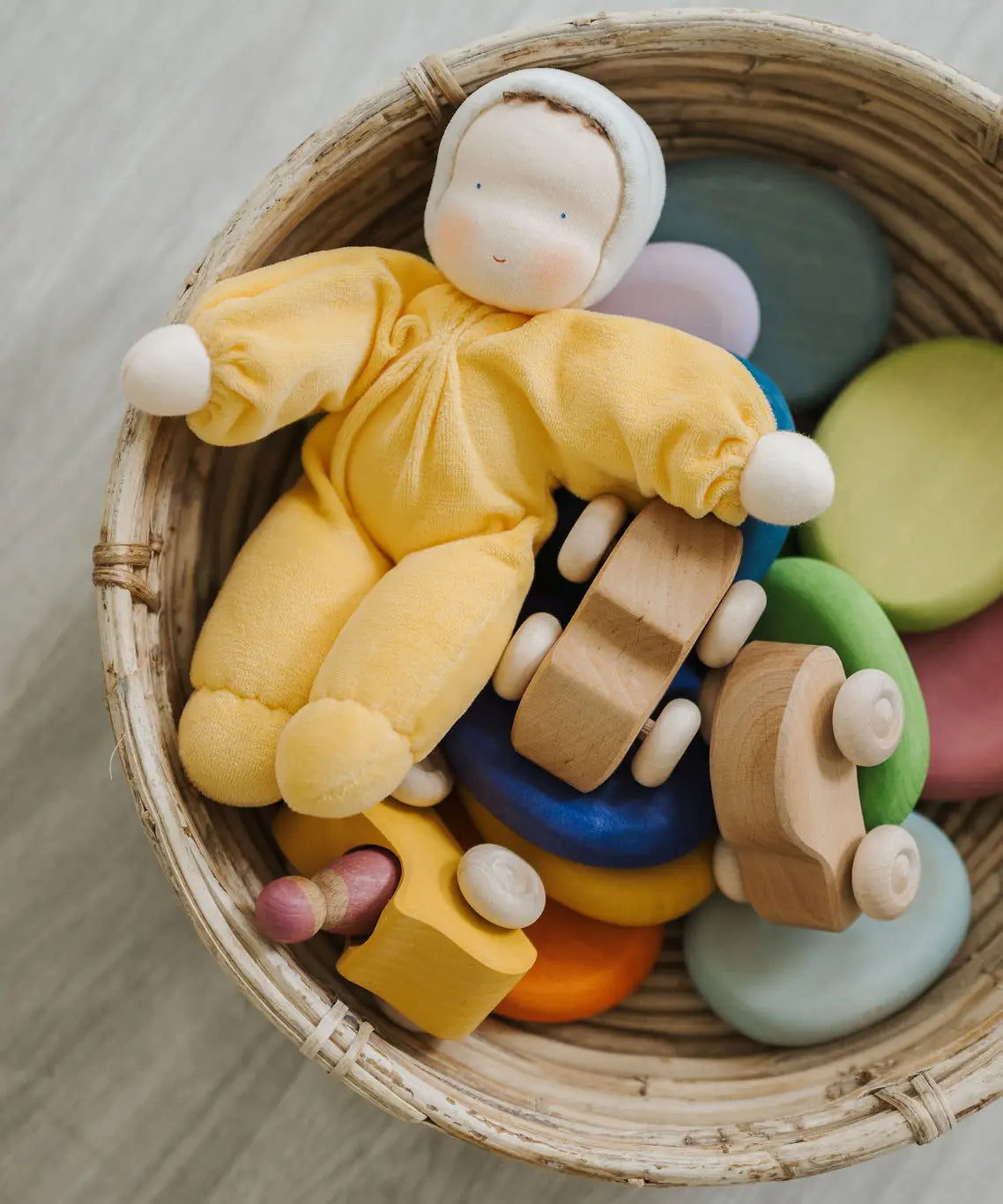 A Grimms yellow soft Waldorf doll in a basket filled with wooden toys