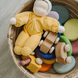 A Grimms yellow soft Waldorf doll in a basket filled with wooden toys