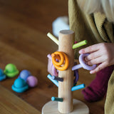 Child putting a purple wooden ring on the matching dowel on the Grimms sorting helper 