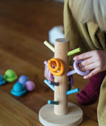 Child putting a purple wooden ring on the matching dowel on the Grimms sorting helper 