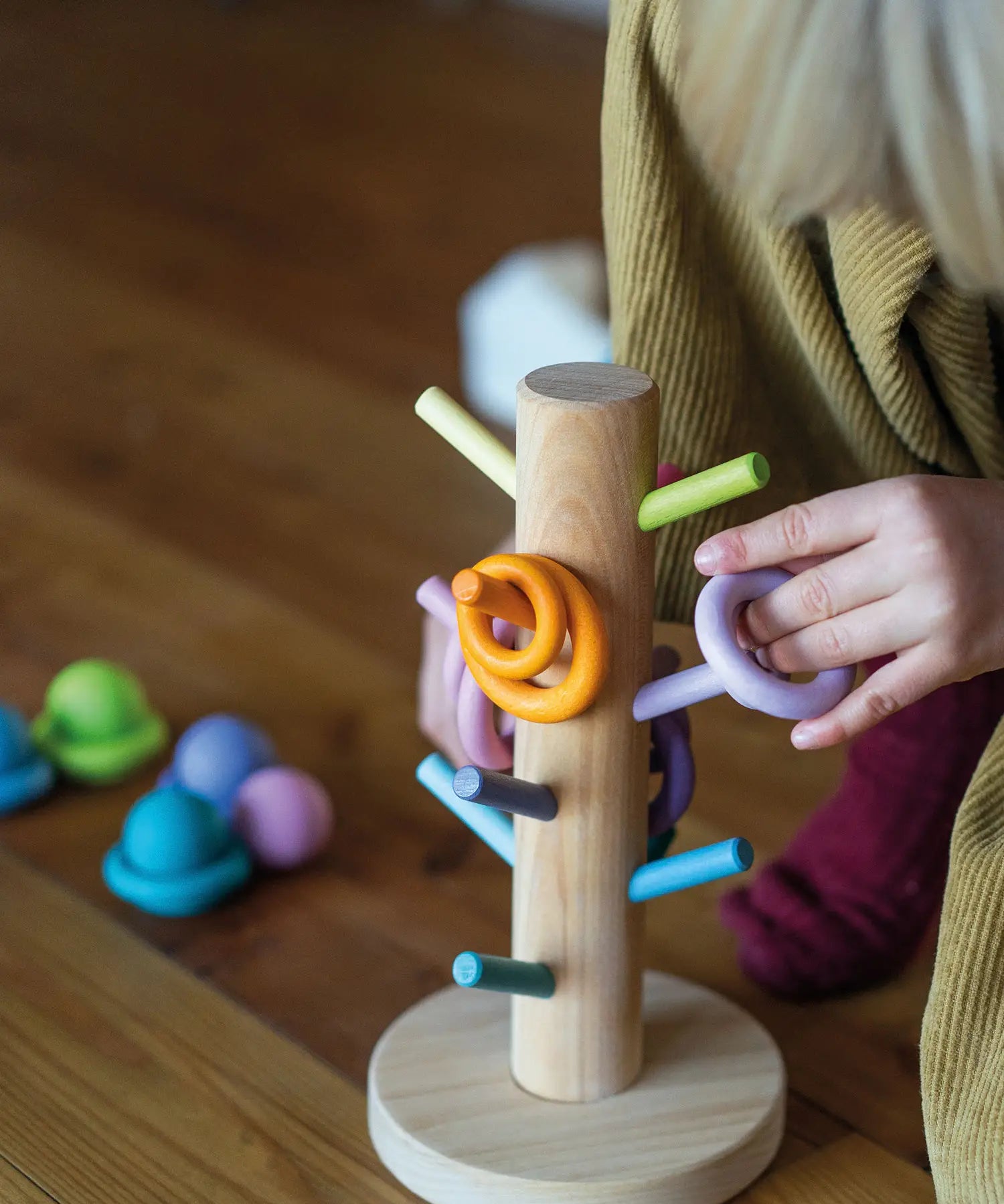 Child putting a purple wooden ring on the matching dowel on the Grimms sorting helper 