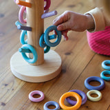 Grimms wooden sorting helper in pastel standing next to matching loose ring pieces and a child holding a blue ring