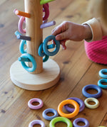 Grimms wooden sorting helper in pastel standing next to matching loose ring pieces and a child holding a blue ring