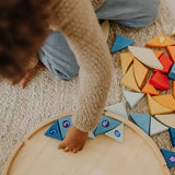 Child lining up blue Grimms sparkling mandala wooden pieces on the circular frame