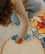 Child lining up blue Grimms sparkling mandala wooden pieces on the circular frame