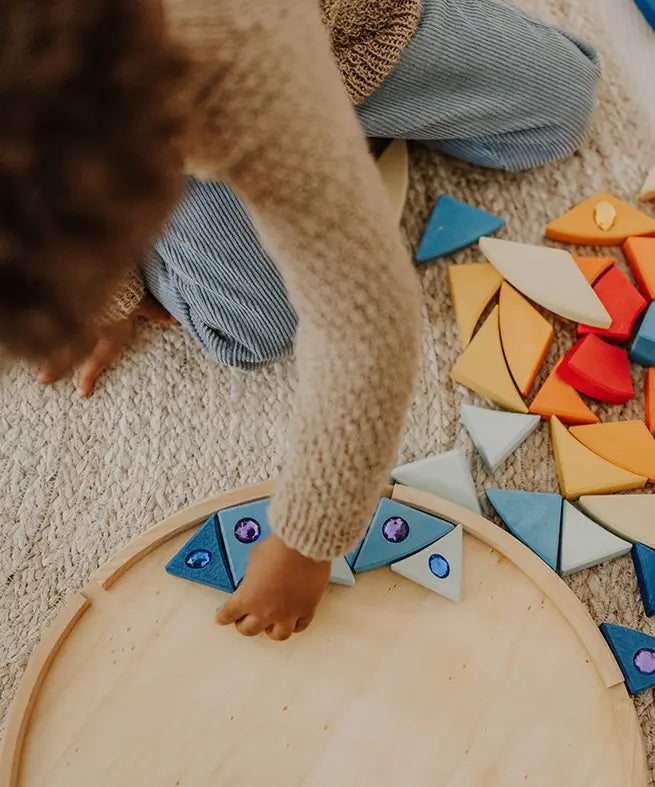 Child lining up blue Grimms sparkling mandala wooden pieces on the circular frame