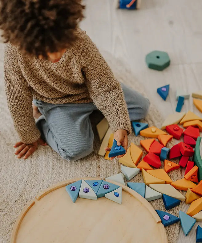 Child holding a blue Grimms sparkling mandala piece above its circular frame