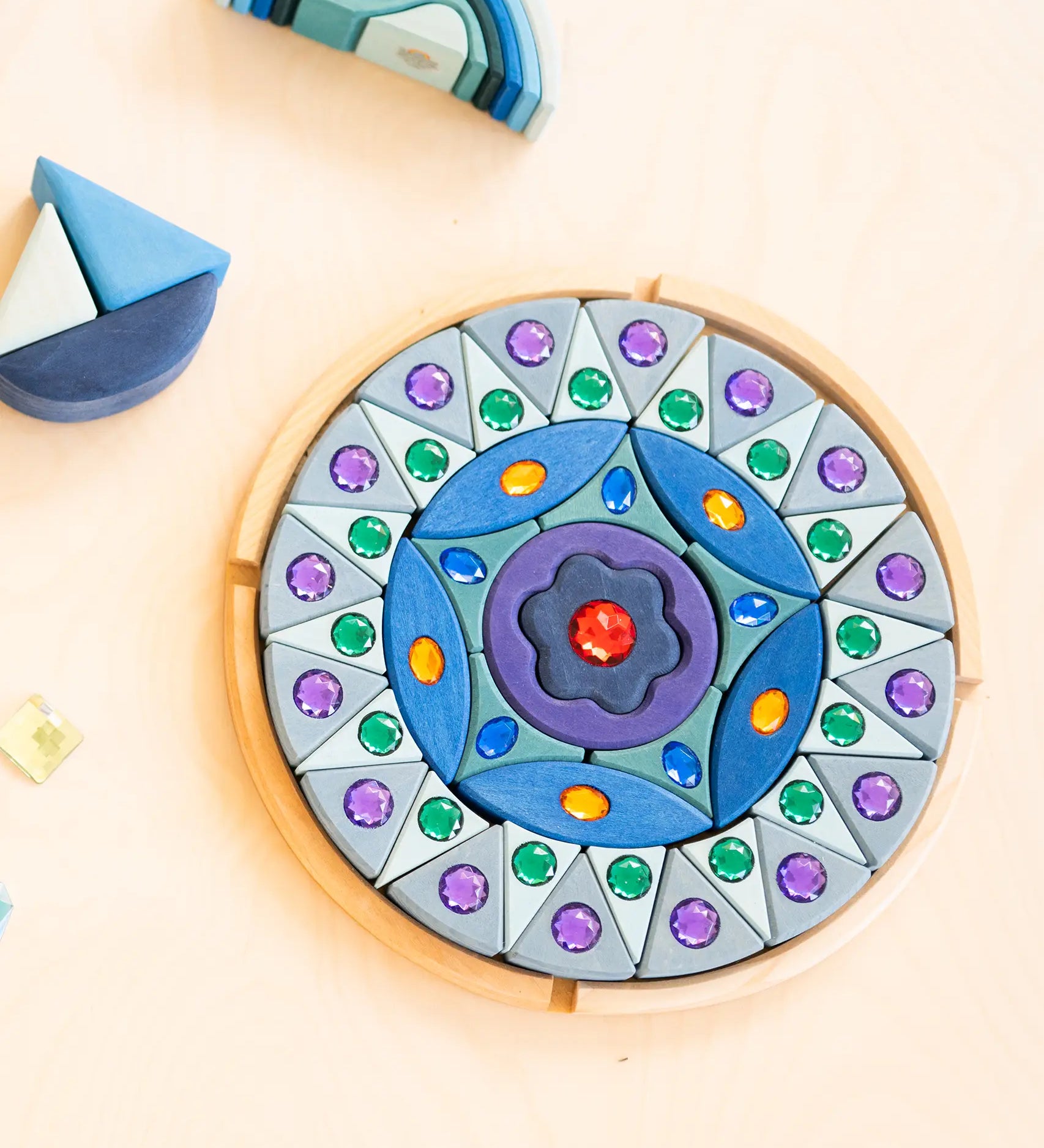 Grimms small sparkling mandala set in a circular wooden frame on a table next to wave shaped blocks