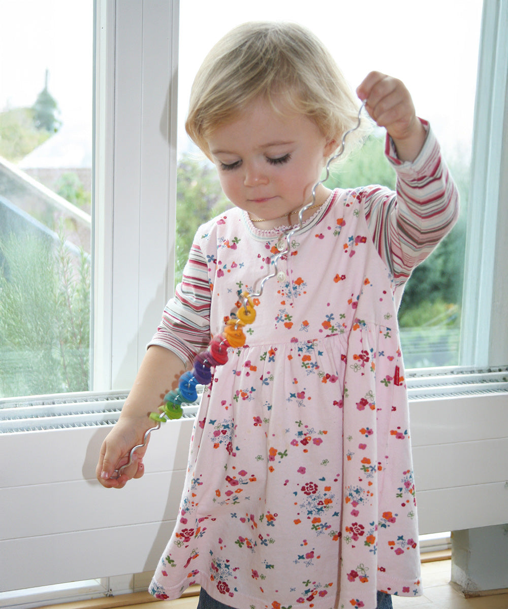 A toddler playing with the Grimms spirelli available at Babipur showing the coloured disks threading through the winding wire