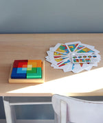 Grimm's square creative set in a wooden storage display tray on a wooden desk next to an open ideas booklet.