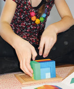 Child playing with the Grimm's square creative set in a wooden storage display tray.