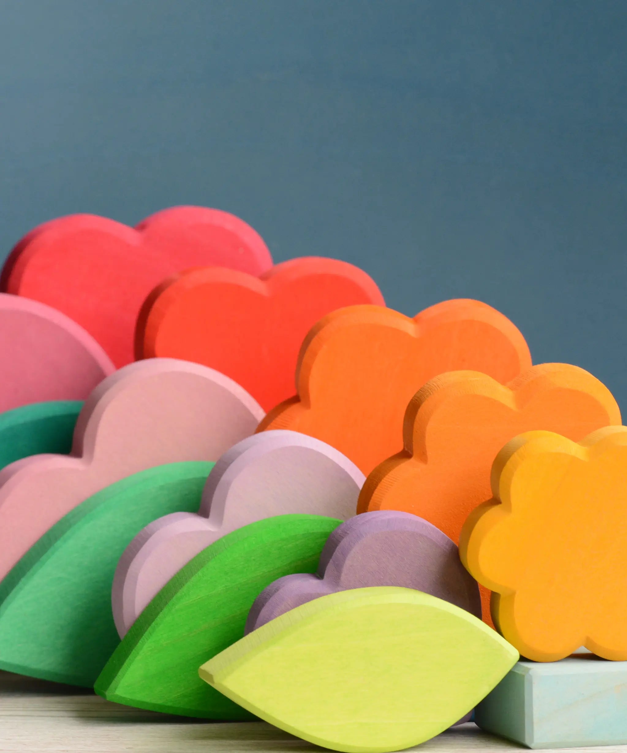 Grimms handcrafted wooden tower showing showing the loose flower, heart and cube pieces in rainbow and pastel palettes.