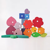 Loose pieces from the Grimms handcrafted wooden stacking tower showing a flower, heart, cube and leaf pieces in different colours