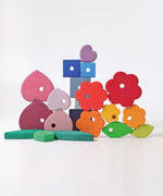 Loose pieces from the Grimms handcrafted wooden stacking tower showing a flower, heart, cube and leaf pieces in different colours