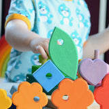 Small child stacking pieces from the Grimms wooden stacking tower with other loose pieces on a table showing scale