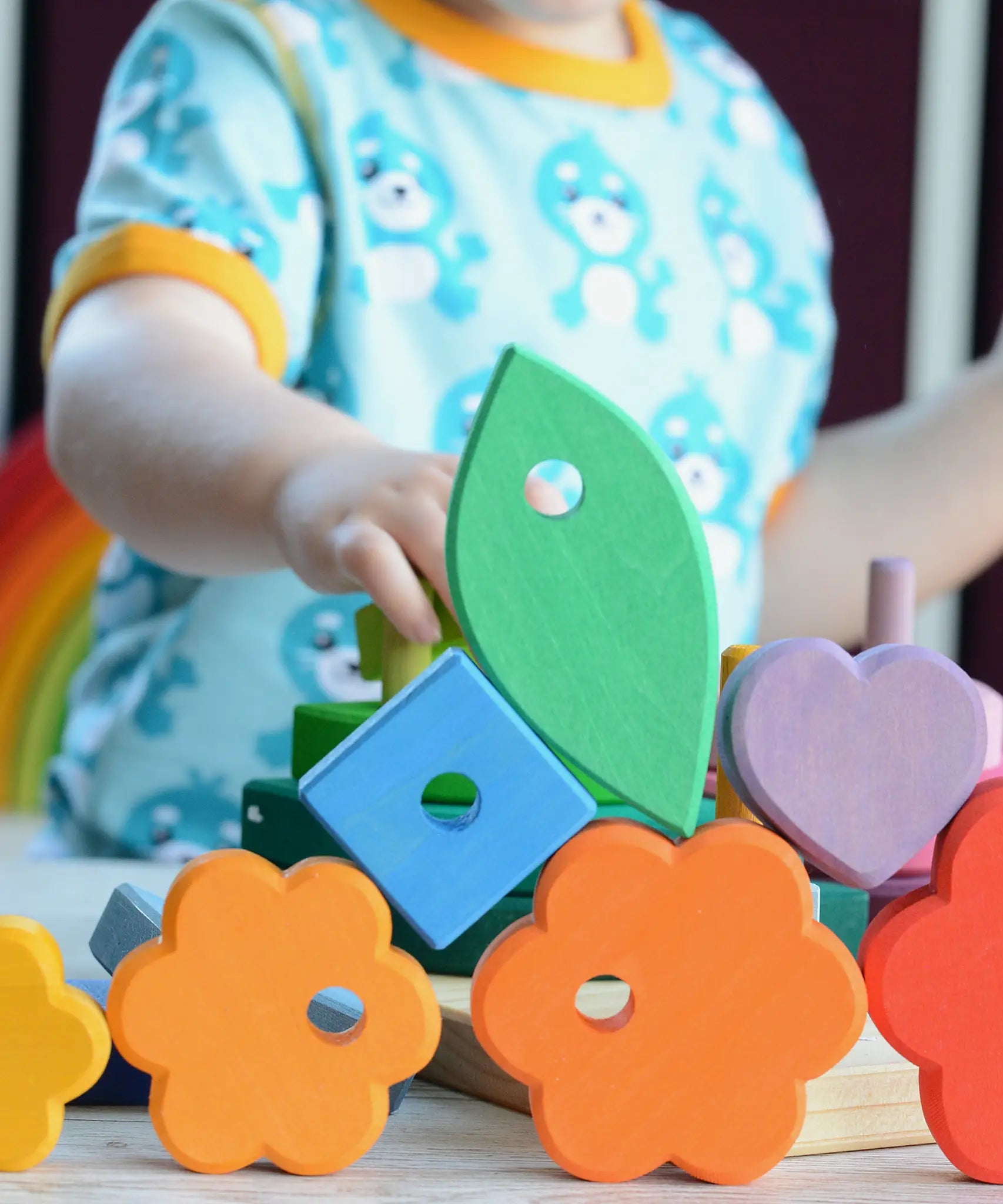 Small child stacking pieces from the Grimms wooden stacking tower with other loose pieces on a table showing scale