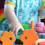 Small child holding pieces from the Grimms wooden stacking tower with other loose pieces on a table showing scale