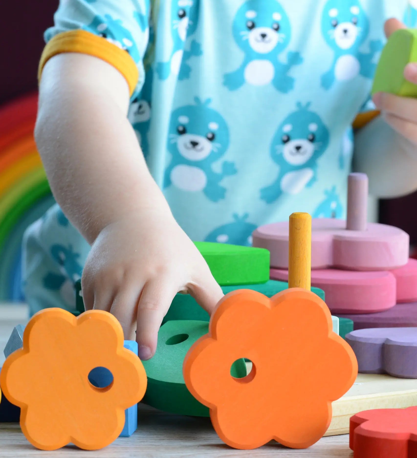 Small child holding pieces from the Grimms wooden stacking tower with other loose pieces on a table showing scale