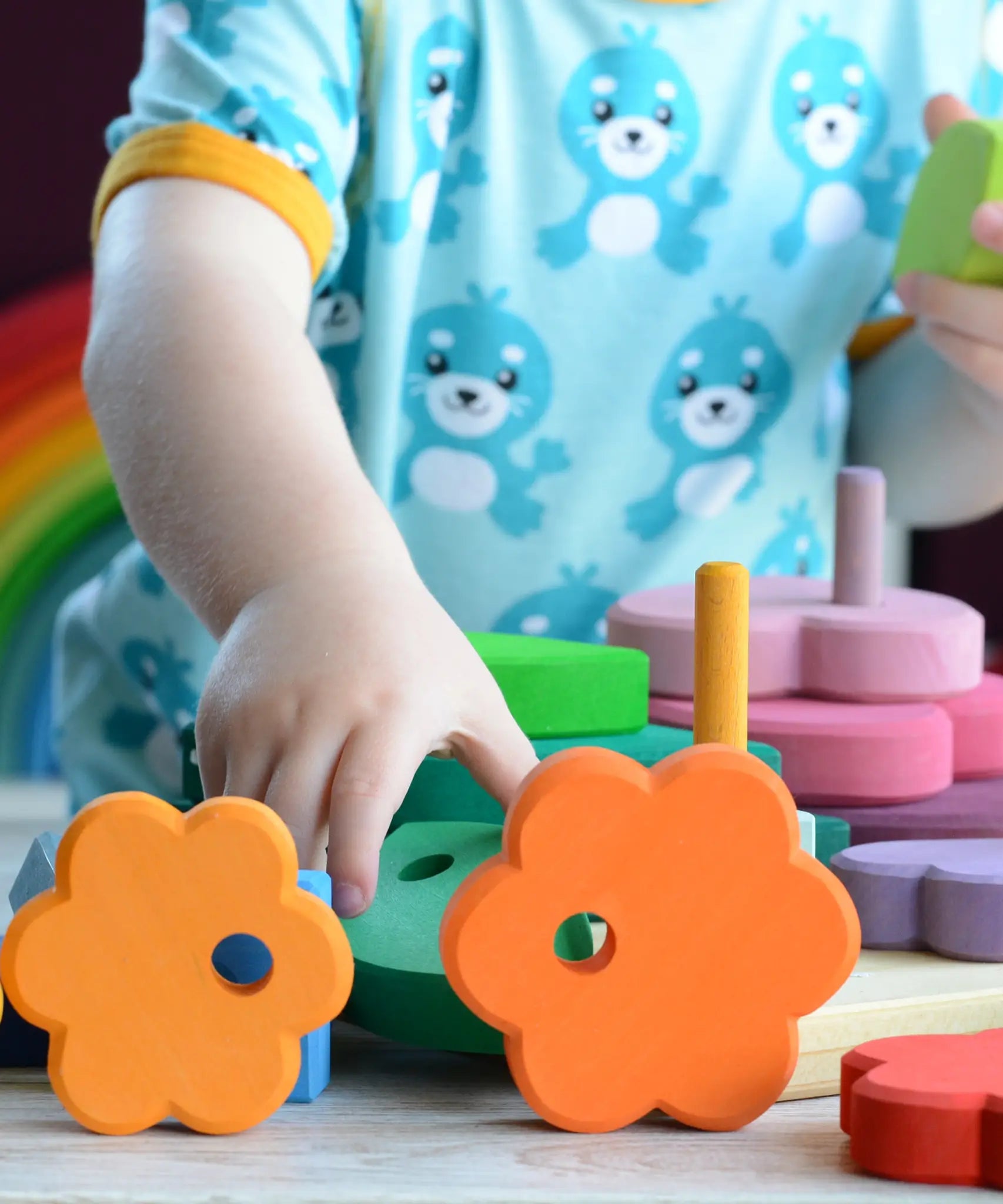 Small child holding pieces from the Grimms wooden stacking tower with other loose pieces on a table showing scale