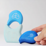 An adult's hand holding the top piece from the Grimm's blue tower drops wooden stacking toy.