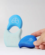 An adult's hand holding the top piece from the Grimm's blue tower drops wooden stacking toy.
