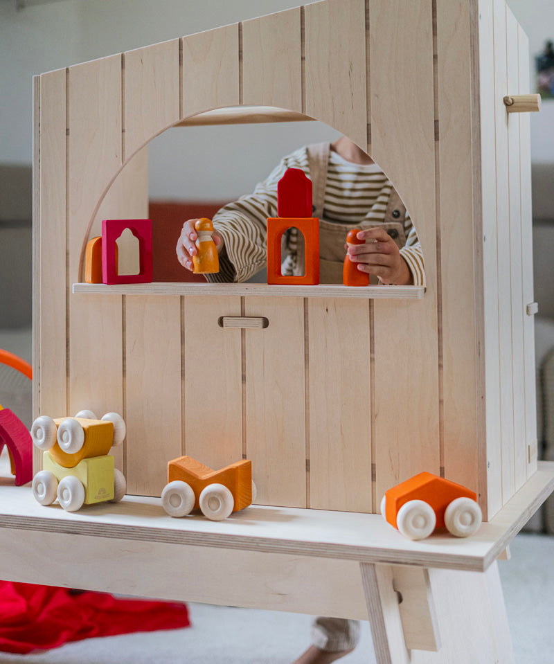 A child playing with wooden peg dolls and Grimm's windows. Grimm's wooden stacking car toys have been placed on a wooden shelf in front. These Grimm's toys are part of a wide range of wooden toys available here at Babipur. 