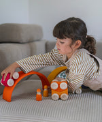 A child playing with the red Grimm's wooden stacking car toy driving it over a Grimm's rainbow piece. These Grimm's toys are part of a wide range of wooden toys available here at Babipur. 