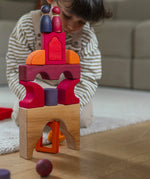A child playing with the Grimm's red car stacking puzzle building block set stacking blocks on top of each other with Grimm's friends on top. These Grimm's toys are part of a wide range of wooden toys available here at Babipur. 