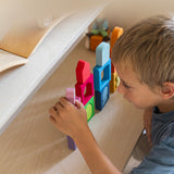 A child playing with the Grimm's Windows Building & Stacking Set. The child is stacking them on top of each other and using the shapes as decorations. These Grimm's toys are part of a wide range of wooden toys available here at Babipur. 
