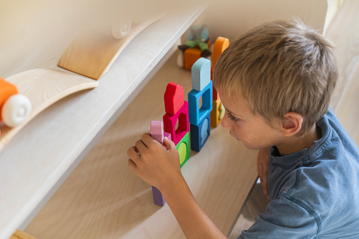 A child playing with the Grimm's Windows Building & Stacking Set. The child is stacking them on top of each other and using the shapes as decorations. These Grimm's toys are part of a wide range of wooden toys available here at Babipur. 