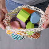 Grimm's tree slices wooden coloured building blocks in their netting storage bag in an adult's hand. 