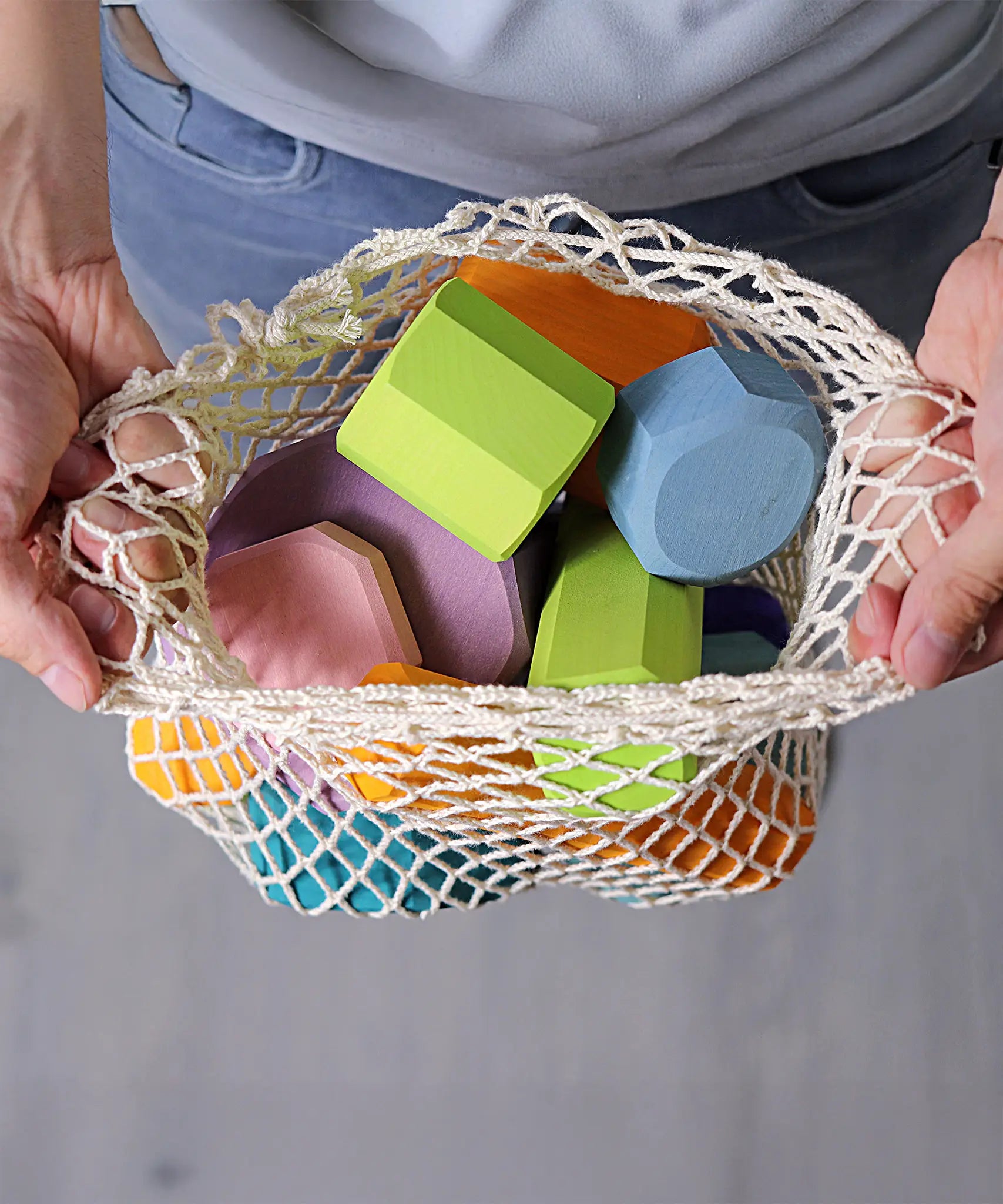 Grimm's tree slices wooden coloured building blocks in their netting storage bag in an adult's hand. 