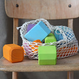 Grimm's tree slices wooden coloured building blocks shown in their netting storage bag placed on a wooden chair. 