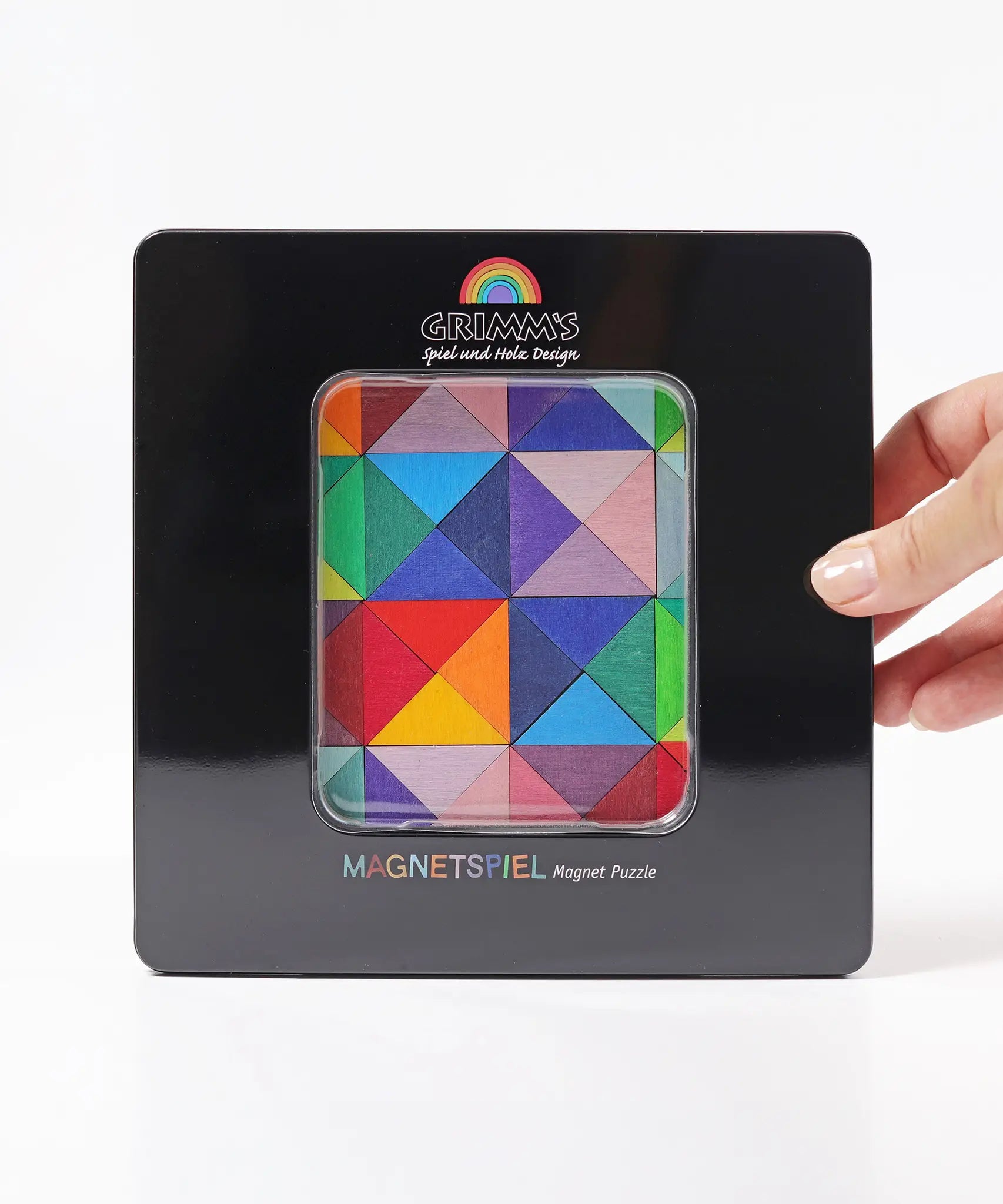A adult hand holding a closed tin with a clear window displaying the Grimm's triangle magnetic set