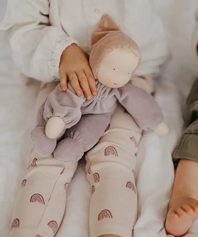 Child with a Grimms soft violet Waldorf doll on their knees
