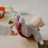 Child hand pushing a Grimms soft violet waldorf doll on a wooden rainbow arch piece
