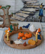 A Grimm's natural celebration ring decorated with Autumn and Halloween themed figures and wooden toys. A Bumbu tree can be seen in the background with a Wonderie trick or treat play cloth hung on the wall behind.  