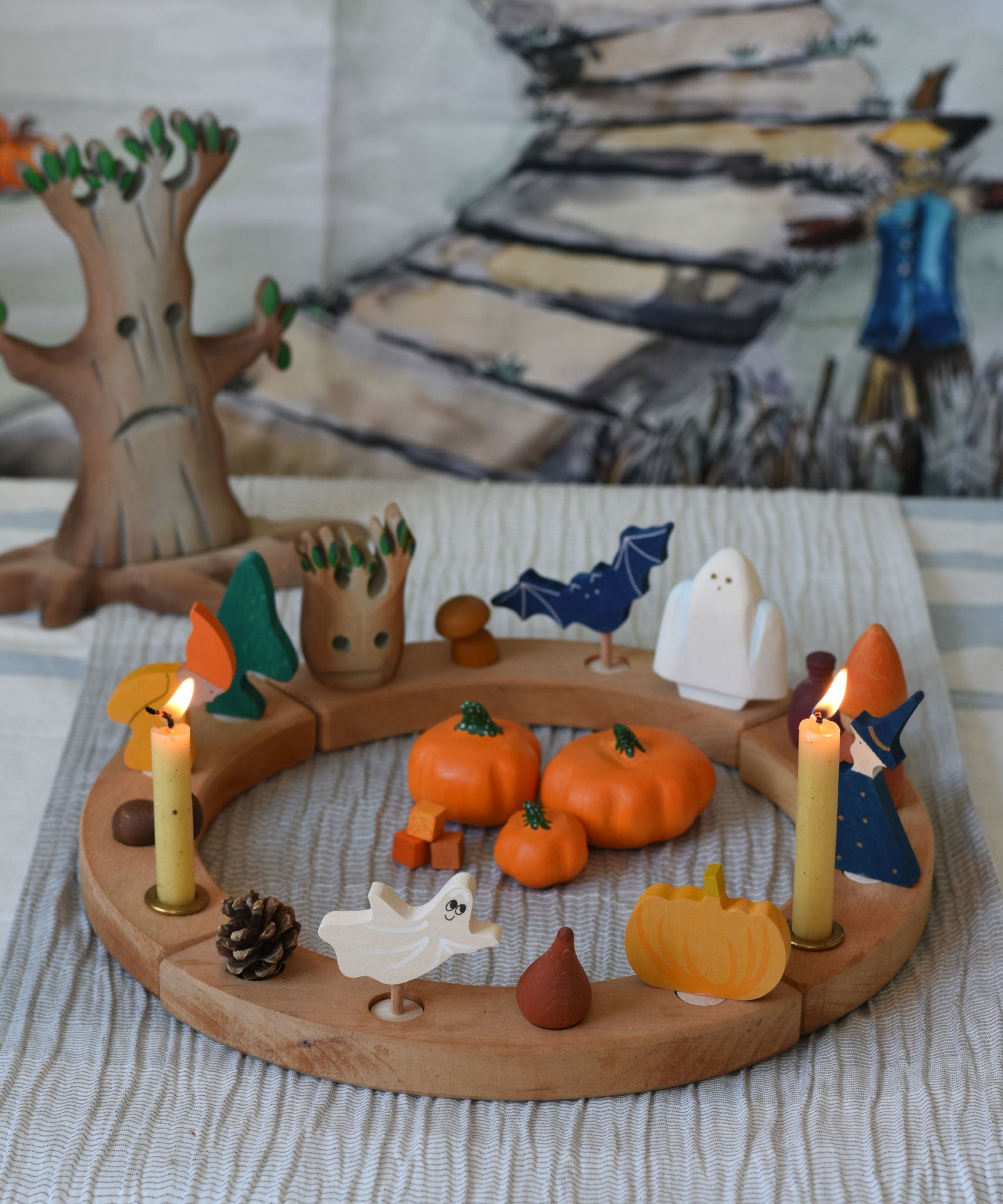 A Grimm's natural celebration ring decorated with Autumn and Halloween themed figures and wooden toys. A Bumbu tree can be seen in the background with a Wonderie trick or treat play cloth hung on the wall behind.  
