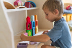 A child playing with the Grimm's Windows Building & Stacking Set. The child is stacking them on top of each other and inserting the shapes into the window frames. These Grimm's toys are part of a wide range of wooden toys available here at Babipur. 