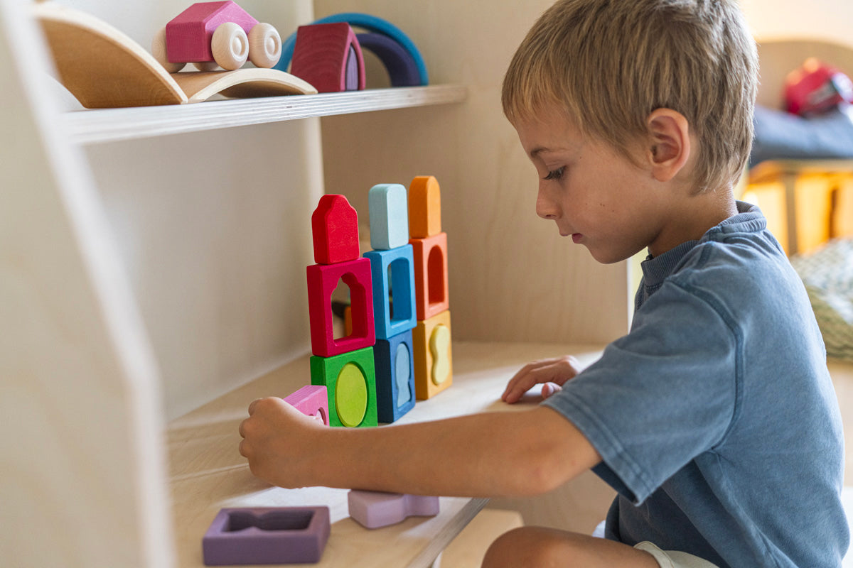 A child playing with the Grimm's Windows Building & Stacking Set. The child is stacking them on top of each other and inserting the shapes into the window frames. These Grimm's toys are part of a wide range of wooden toys available here at Babipur. 