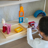A child playing with the Grimm's Windows Building & Stacking Set. The child is holding the purple coloured window piece in their hand taking the shaped inset out of the window frame. These Grimm's toys are part of a wide range of wooden toys available here at Babipur. 