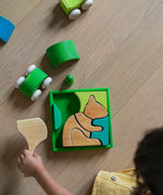 An overhead view of a child playing with the Grimm's green squirrel Building Set. Wooden blocks in various shades of green and natural wood in a green coloured wooden storage tray. These Grimm's toys are part of a wide range of wooden toys available here at Babipur. 