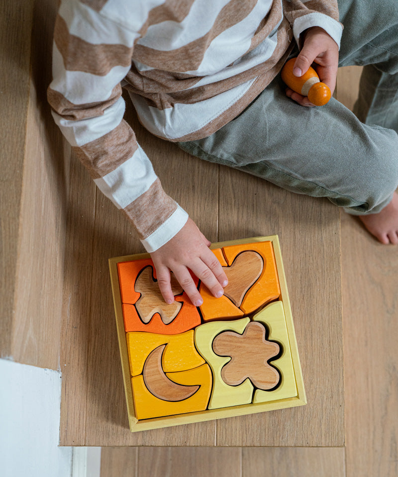 A child playing with the Grimm's Building Set in Yellow. Wooden blocks in various shades of yellow and natural wood in a yellow coloured wooden storage tray. These Grimm's toys are part of a wide range of wooden toys available here at Babipur. 