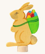 Grimms wooden rabbit decorative figure holding a green basket full of eggs. Hand cut and hand painted, features a small base stand on the bottom to slot in a celebration ring